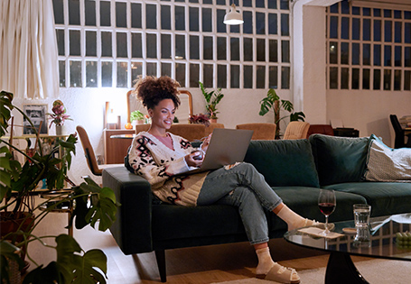 A Black woman sitting on her couch and viewing her laptop