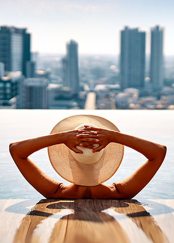 A woman in a sun hat relaxing in a pool overlooking a city