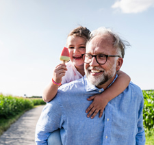 An smiling, older man with his smiling granddaughter on his back eating a popsicle