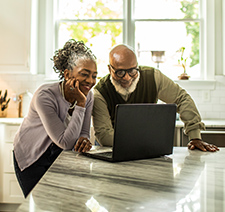 An older Black couple looking at travel results on a laptop