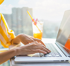 A woman's hands typing on a laptop with a fruity drink in the background