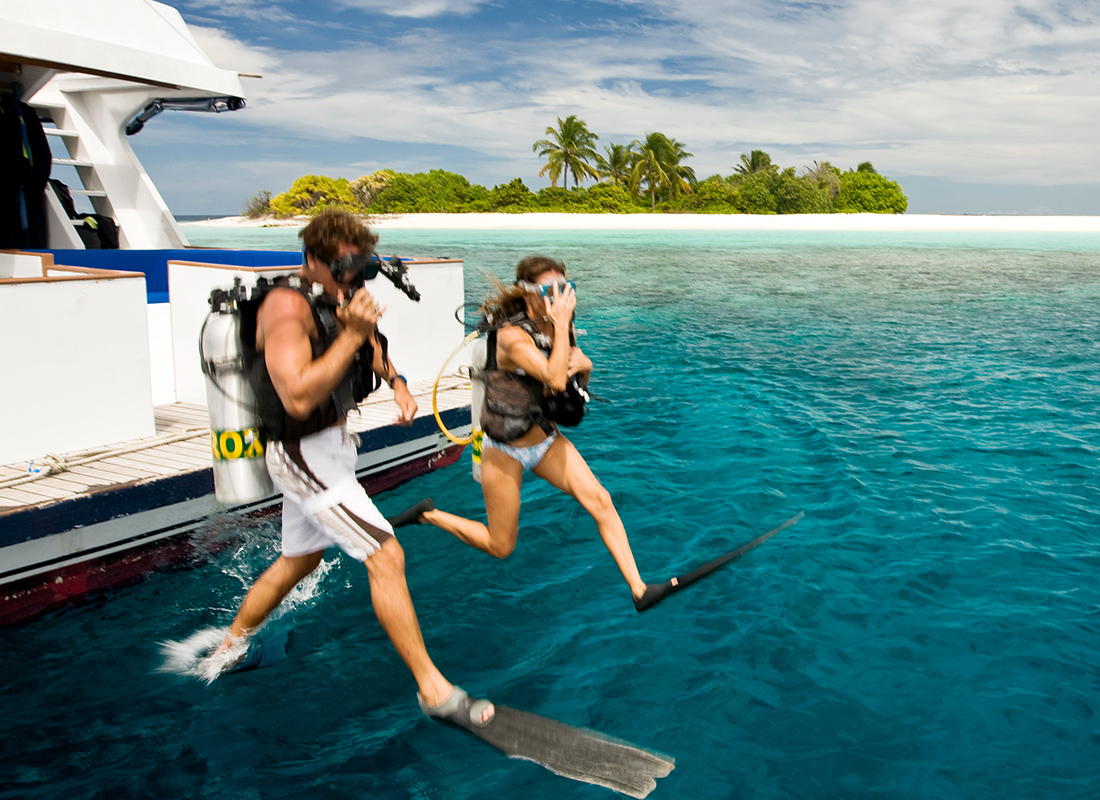 A couple in scuba gear diving into the water from a boat