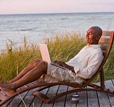 An older Black man in a lounger on his laptop at dusk