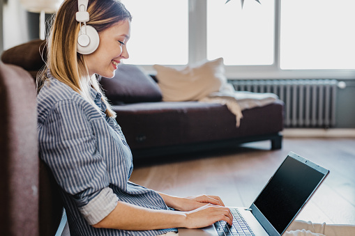 A young lady in headphones sitting on the floor looking at her laptop