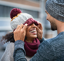 A smiling man and woman in winter wear with the woman's hat covering her eyes